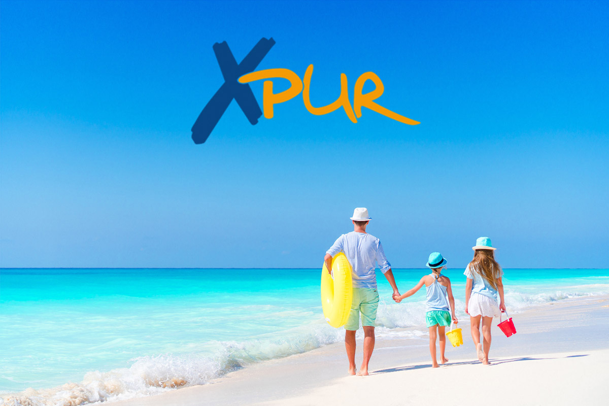 Eine Familie läuft mit Schwimmring am weißen Sandstrand entlang. Im Hintergrund leuchtet das türkisblaue Meer, während eine leichte Brise für sommerliche Stimmung sorgt.